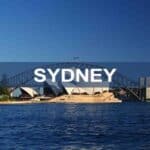 Sydney Harbour Bridge and Sydney Opera House skyline with water in foreground, iconic Australian landmarks, clear blue sky, tourism, architecture, cityscape, travel destination.